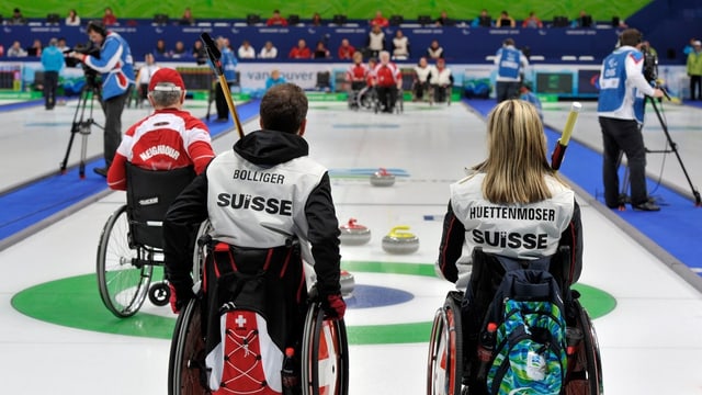 Blick über ein Curlingspielfeld. Im Vordergrund zwei Rollstuhlfarer, hinten Curlingsteine. Blick über ein Curlingspielfeld. Im Vordergrund zwei Rollstuhlfarer, hinten Curlingsteine.