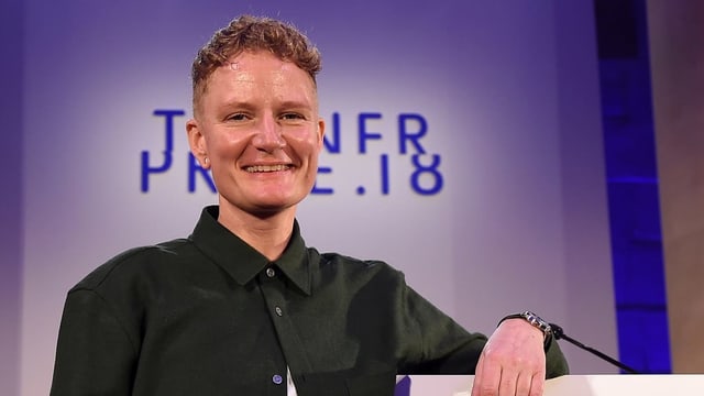 Frau posiert lächelnd vor einer Wand mit dem Schriftzug "Turner Prize 18" Frau posiert lächelnd vor einer Wand mit dem Schriftzug "Turner Prize 18"