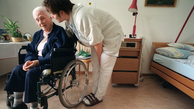 Pflegerin hinter alter Frau im Rollstuhl
