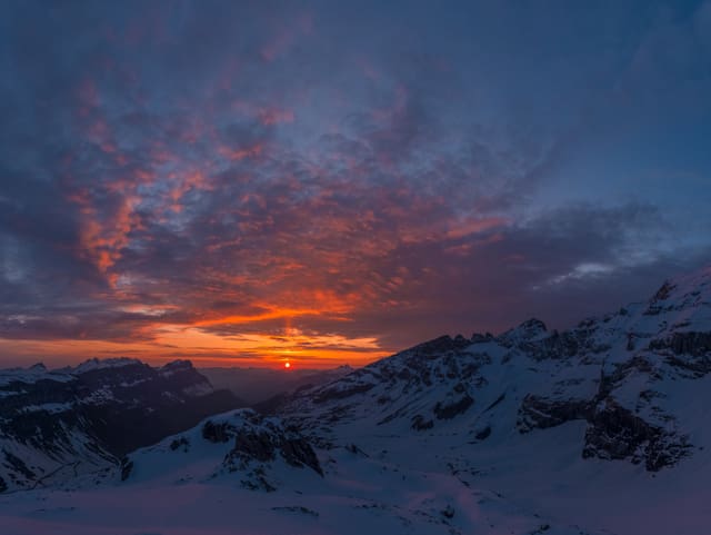 Sonnenaufgang vom Gebirge aus mit rotem und gelbem Horizont und einigen Wolken.