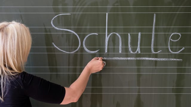 Eine Frau schreibt Schule an die Wandtafel Eine Frau schreibt Schule an die Wandtafel