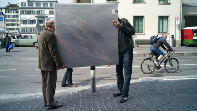 Zwei Männer tragen ein verhülltes Gemälde über eine Strasse. Zwei Männer tragen ein verhülltes Gemälde über eine Strasse.