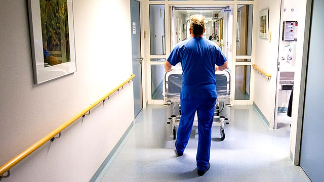 Ein Pflegehelfer schiebt ein Bett durch einen Spitalgang. Ein Pflegehelfer schiebt ein Bett durch einen Spitalgang.