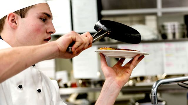 Ein Koch gibt die Rösti von der Pfanne auf den Teller. Ein Koch gibt die Rösti von der Pfanne auf den Teller.