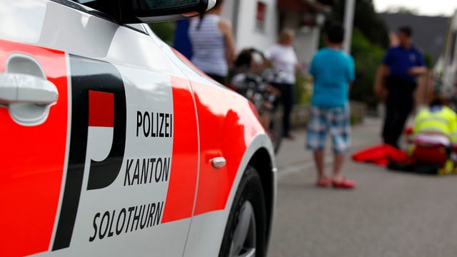 Polizeiauto in einer Quartierstrase, dahinter stehen Schaulustige und beobachten einen Unfall. Polizeiauto in einer Quartierstrase, dahinter stehen Schaulustige und beobachten einen Unfall.