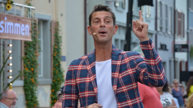 Roman Kilchsperger zeigt mit dem Zeigefinger nach oben und lächelt verschmitzt.