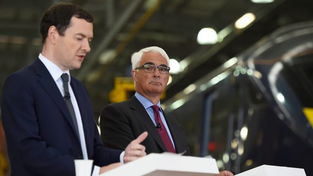 Osborne und Darling sprechen an zwei weissen Rednerpulten in der Halle einer Zugfabrik. Osborne und Darling sprechen an zwei weissen Rednerpulten in der Halle einer Zugfabrik.