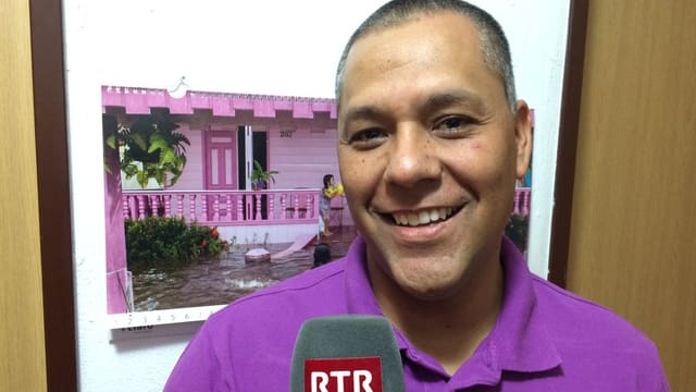 Alejandro Arias Linares ha en maun in microfon dad RTR. El surri e la camera. Davostiers in chalender cun ina chasa rosa. A Alejandro Arias Linares ha en maun in microfon dad RTR. El surri e la camera. Davostiers in chalender cun ina chasa rosa. A