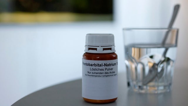 Symbolbild: Eine Medikamentendose, angeschrieben mit Pentobarbital Natrium, daneben steht ein Glas Wasser mit einem Löffel. Symbolbild: Eine Medikamentendose, angeschrieben mit Pentobarbital Natrium, daneben steht ein Glas Wasser mit einem Löffel.