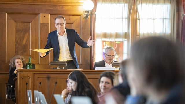 Ein Mann steht im Rathaus hinter dem Rednerpult und spricht zum Parlament. Ein Mann steht im Rathaus hinter dem Rednerpult und spricht zum Parlament.