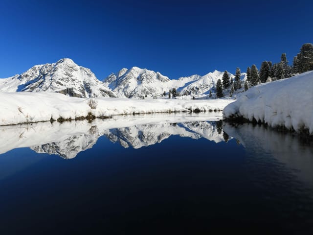 Blick auf weisse Berge und im Vordergrund ein Gewässer.
