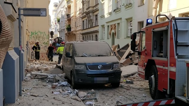 Man sieht ein schwarzes Auto und ein Feuerwehrautto auf einer Strasse. Trümmer und Staub liegen herum. Man sieht ein schwarzes Auto und ein Feuerwehrautto auf einer Strasse. Trümmer und Staub liegen herum.