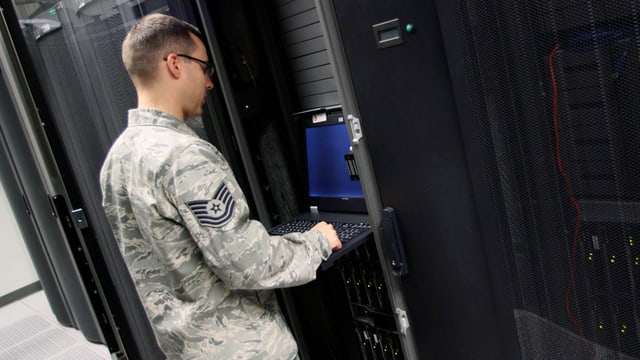 Ein Unteroffizier steht an einem Terminal vor einer Serverwand. Ein Unteroffizier steht an einem Terminal vor einer Serverwand.