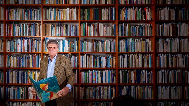 Ein Mann steht mit einem Buch vor einem riesen Bücherregal. Ein Mann steht mit einem Buch vor einem riesen Bücherregal.
