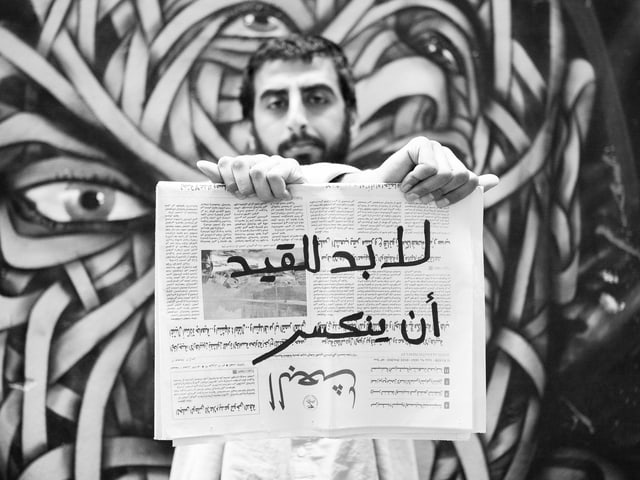 Ein Mann mit Bart hält eine arabischsprachige Zeitung vor sich. Ein Mann mit Bart hält eine arabischsprachige Zeitung vor sich.