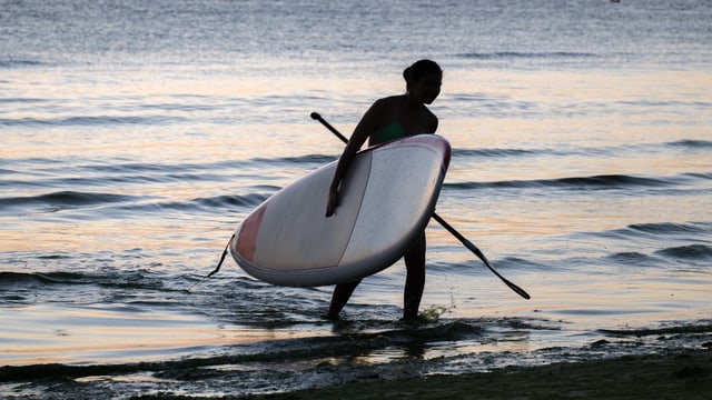 Frau mit SUP-Ausrüstung verlässt das Wasser. Frau mit SUP-Ausrüstung verlässt das Wasser.