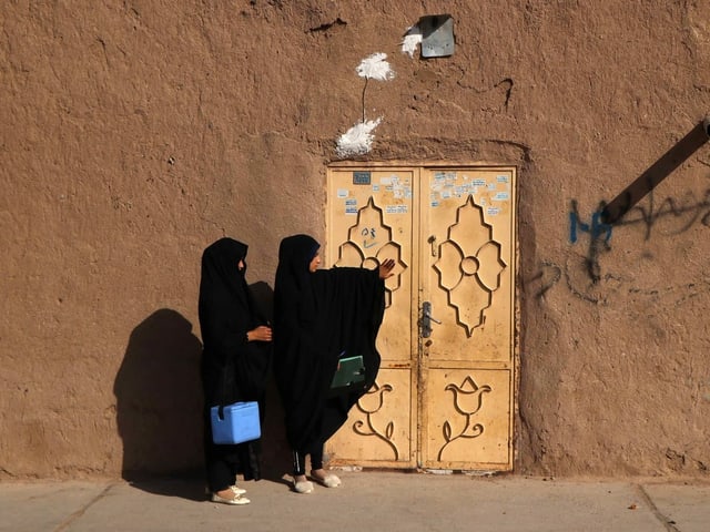 Zwei Frauen tragen eine blaue Kühlbox (vermutlich mit einer Polioimpfung darin) zu einer Haustüre. Beide Frauen tragen eine Burka. Zwei Frauen tragen eine blaue Kühlbox (vermutlich mit einer Polioimpfung darin) zu einer Haustüre. Beide Frauen tragen eine Burka.