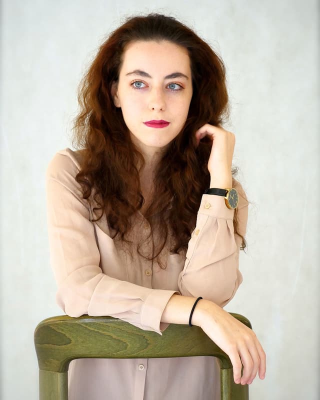Eine junge Frau mit langem Haar stützt sich auf die grüne Lehne eines Stuhls. Eine junge Frau mit langem Haar stützt sich auf die grüne Lehne eines Stuhls.