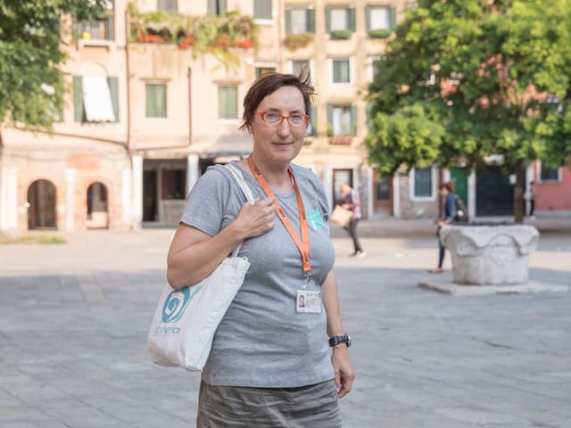 Eine Frau im grauen T-Shirt steht auf einem Platz. Eine Frau im grauen T-Shirt steht auf einem Platz.