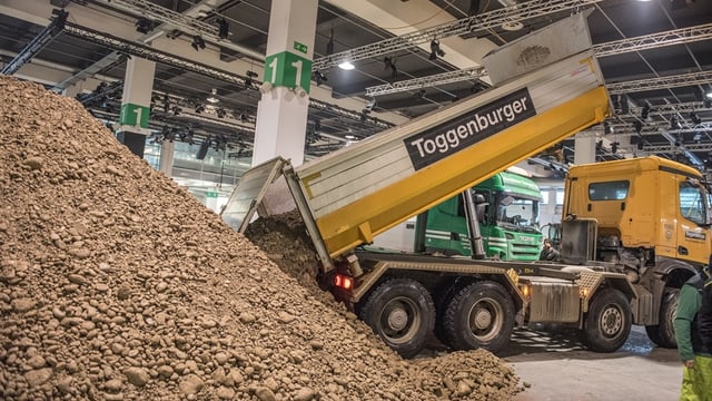 Ein Lastwagen kippt Erde auf einen grossen Haufen in der Messehalle Ein Lastwagen kippt Erde auf einen grossen Haufen in der Messehalle