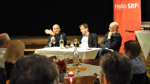Drei Männer sitzen an einem Tisch. Im Hintergrund das Hallo SRF Logo Drei Männer sitzen an einem Tisch. Im Hintergrund das Hallo SRF Logo