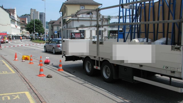 Bild der Unfallstelle. Orange Pylonen der Polizei kennzeichnen Spuren am Boden. Anhänger des Lastwagens steht danebe.