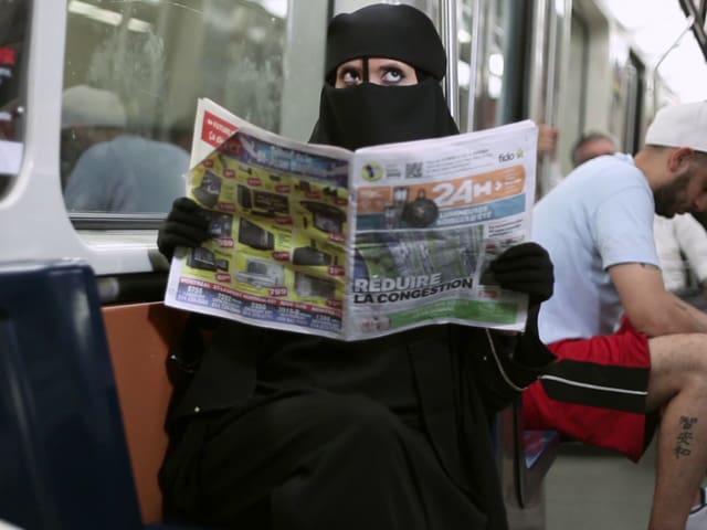 Ein Frau in Burka sitzt in einer U-Bahn und liest Zeitung Ein Frau in Burka sitzt in einer U-Bahn und liest Zeitung