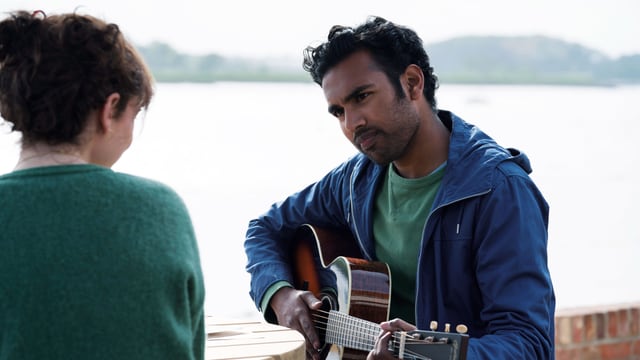 Ein Mann spielt am Strand Gitarre, eine Frau schaut ihm dabei zu. Ein Mann spielt am Strand Gitarre, eine Frau schaut ihm dabei zu.