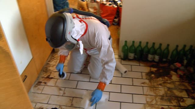Ein Mann mit Atemmaske und Schutzanzug putzt den Boden in einer Wohnung. Ein Mann mit Atemmaske und Schutzanzug putzt den Boden in einer Wohnung.