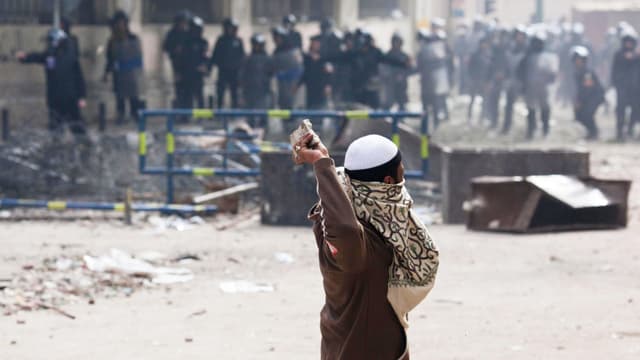 Ein Mann wirft Steine auf Polizisten. Die Szene spielt sich in Kairo ab. Ein Mann wirft Steine auf Polizisten. Die Szene spielt sich in Kairo ab.