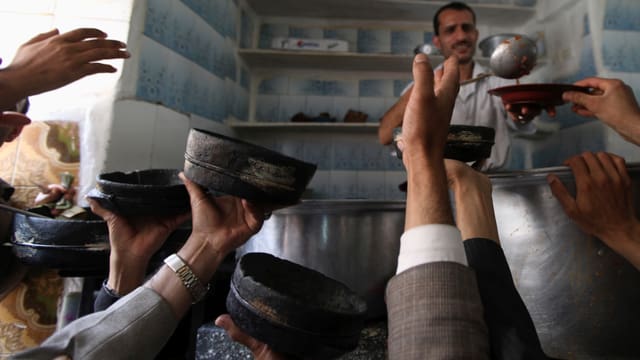 Menschen halten Schüssel für eine Portion des Gerichts Al-Saltah in einem Restaurant in Sanaa.