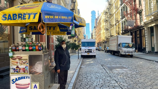 Ein Mann steht am Strassenrand neben einem Essensstand für Hot Dogs. Ein Mann steht am Strassenrand neben einem Essensstand für Hot Dogs.