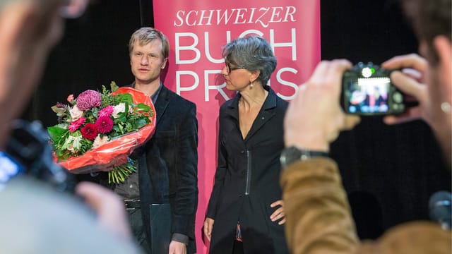 Ein Mann mit Blumenstrauss in der Hand und eine Frau werden aus Distanz fotografiert. Ein Mann mit Blumenstrauss in der Hand und eine Frau werden aus Distanz fotografiert.