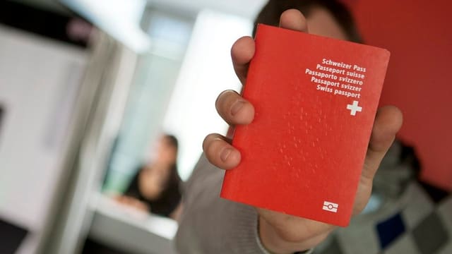 Ein Mann hält einen Schweizer Pass in die Kamera, sein Gesicht ist dahinter verborgen. Ein Mann hält einen Schweizer Pass in die Kamera, sein Gesicht ist dahinter verborgen.