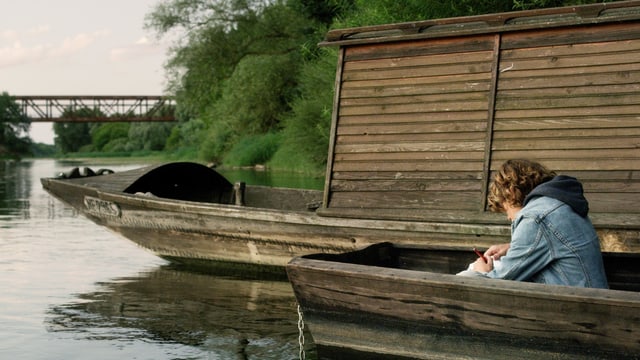 Ein Knabe sitzt auf einem Fluss in einem Holzboot. Ein Knabe sitzt auf einem Fluss in einem Holzboot.