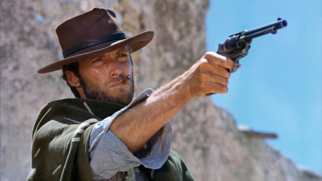 EIn Mann mit Cowboyhut, Poncho und Cigarillo zielt mit einer Pistole. EIn Mann mit Cowboyhut, Poncho und Cigarillo zielt mit einer Pistole.