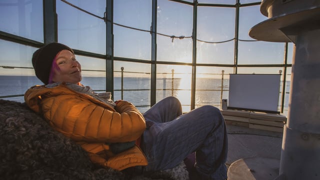 Frau mit oranger Jacke sitzt im Leuchtturm vor Sonnenuntergang Frau mit oranger Jacke sitzt im Leuchtturm vor Sonnenuntergang