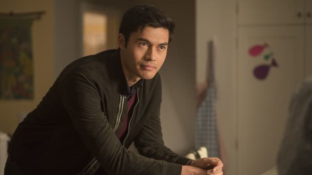 Auf dem Bild ist Henry Golding auf einen Stuhl gestützt zu sehen. Auf dem Bild ist Henry Golding auf einen Stuhl gestützt zu sehen.