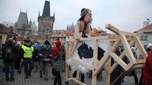 Der Umzug nach Vorbild der Basler Fasnacht auf der Prager Karlsbrücke im November 2012. Figuren mit Larven und Kostümen im selbstgebauten Wagen und Trommler. Am Rand stehen Zuschauer. 