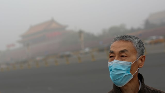 Mann mit Maske, es ist rauchig. Hinten sieht man ein chinesisches Gebäude. Mann mit Maske, es ist rauchig. Hinten sieht man ein chinesisches Gebäude.