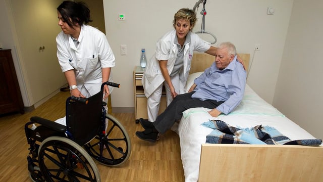 Pflegerinnen in einem Pflegeheim helfen einem pflegebedürftigen Senior aus dem Bett. Pflegerinnen in einem Pflegeheim helfen einem pflegebedürftigen Senior aus dem Bett.
