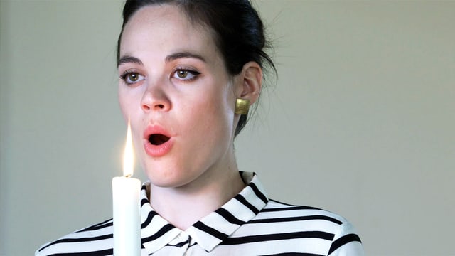 Eine Frau in einer schwarz-weiss-gestreiften Bluse singt vor einer brennenen weissen Kerze.