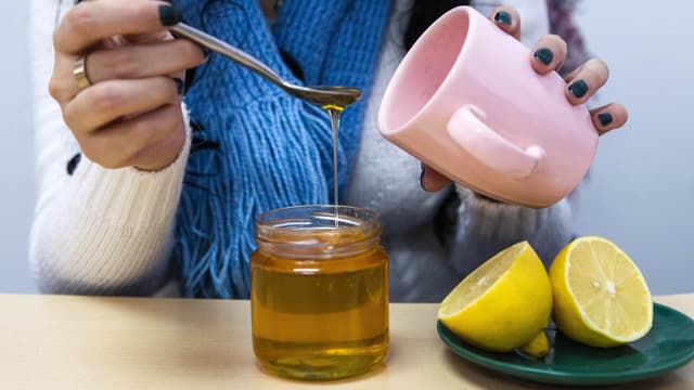 Frau löffelt Honig in eine Teetasse Frau löffelt Honig in eine Teetasse