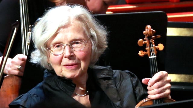 Eine Frau mit weissem Haar sitzt in einem Orchester Eine Frau mit weissem Haar sitzt in einem Orchester