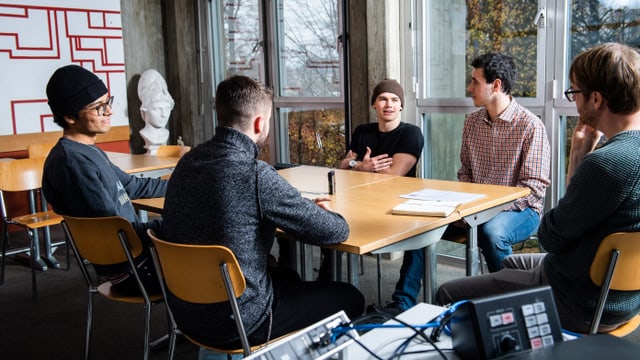 Fünf Männer sitzen in einem Schulzimmer um einen Tisch. Fünf Männer sitzen in einem Schulzimmer um einen Tisch.
