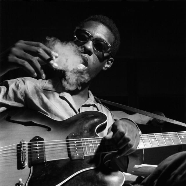 Grant Green raucht und hält eine Gitarre. Grant Green raucht und hält eine Gitarre.
