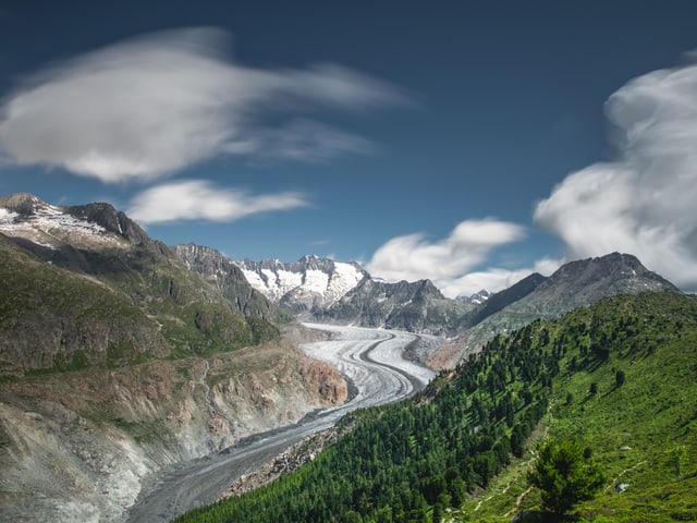 Alpenwelt mit Gletscher, Sonne und nur wenigen Wolken am Himmel.