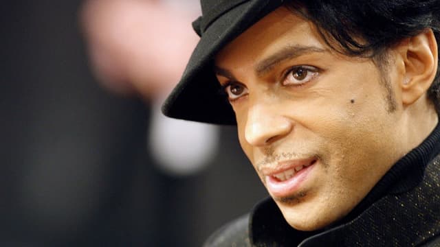 Nahaufnahme von Prince; sanft geschminkt, mit Hut, wacher Blick.