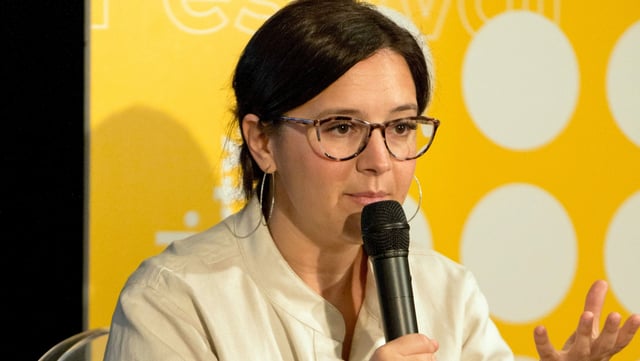 Bari Weiss (mit Brille) spricht in ein Mikrofon. Bari Weiss (mit Brille) spricht in ein Mikrofon.