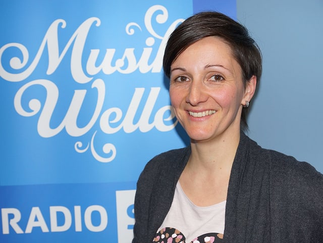 Frau steht vor Musikwelle-Logo. Frau steht vor Musikwelle-Logo.